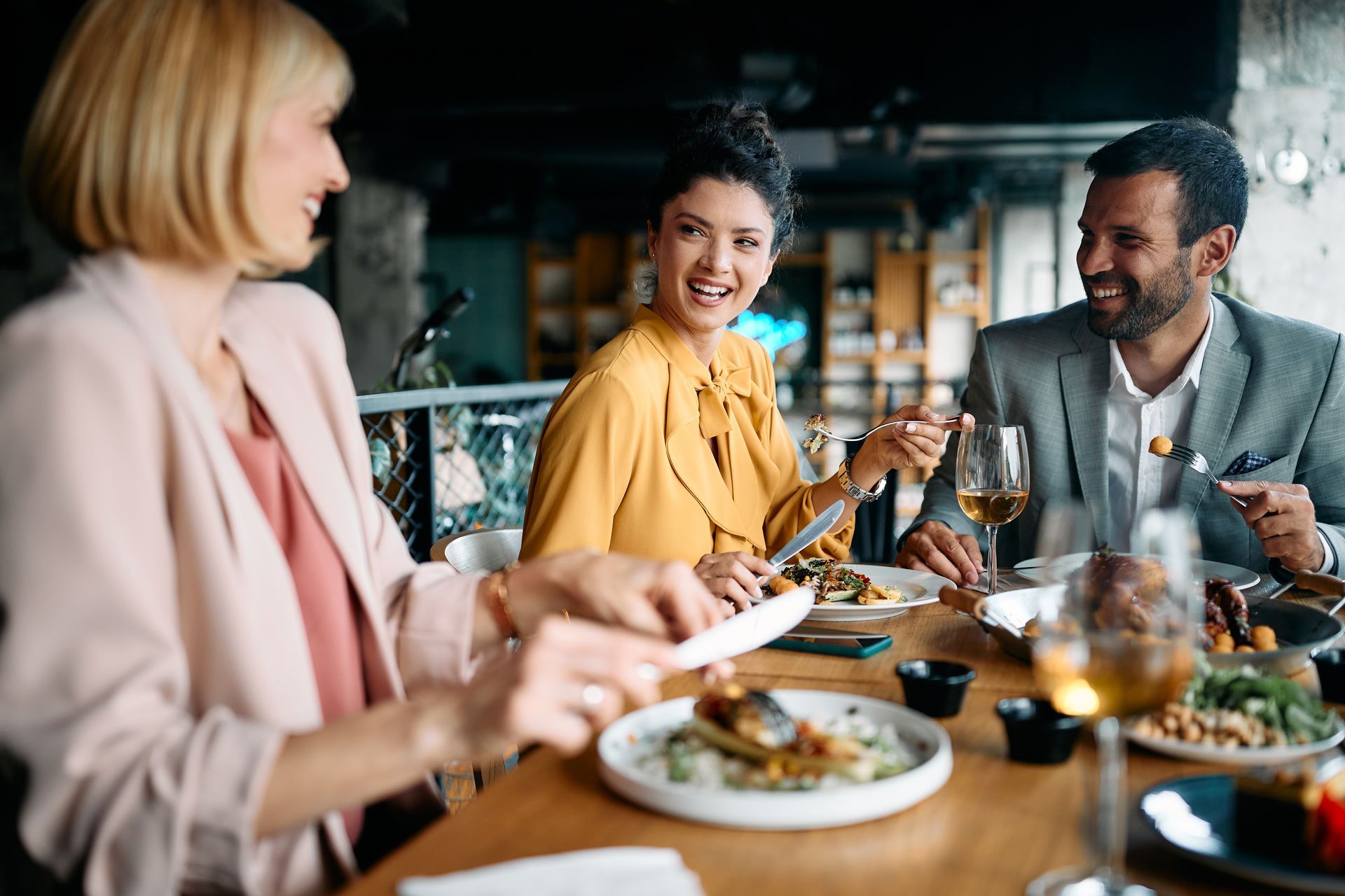 Trois personnes sourient et mangent à une table de restaurant.