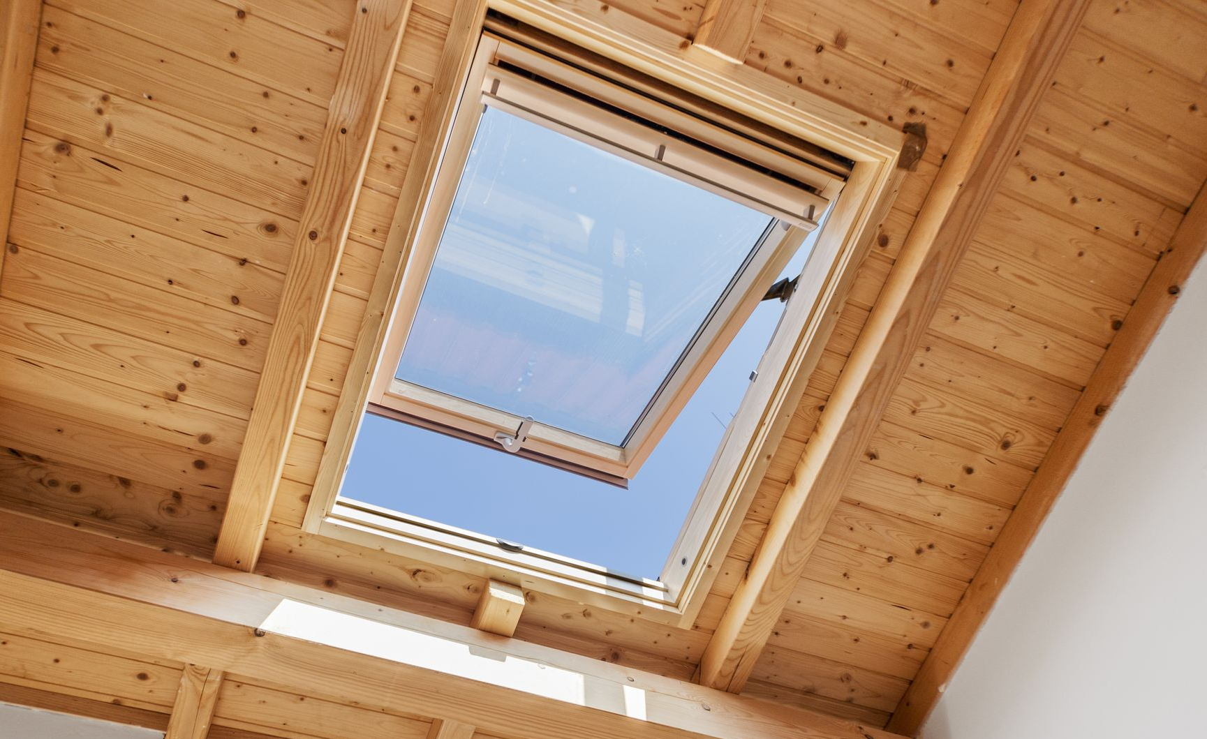 Plafond en bois avec une lucarne ouverte laissant apparaître le ciel bleu et les nuages