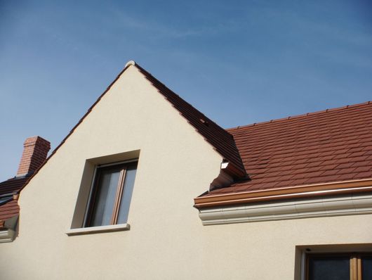Façade de maison couleur crème avec un toit de tuiles rouges et un ciel bleu au-dessus