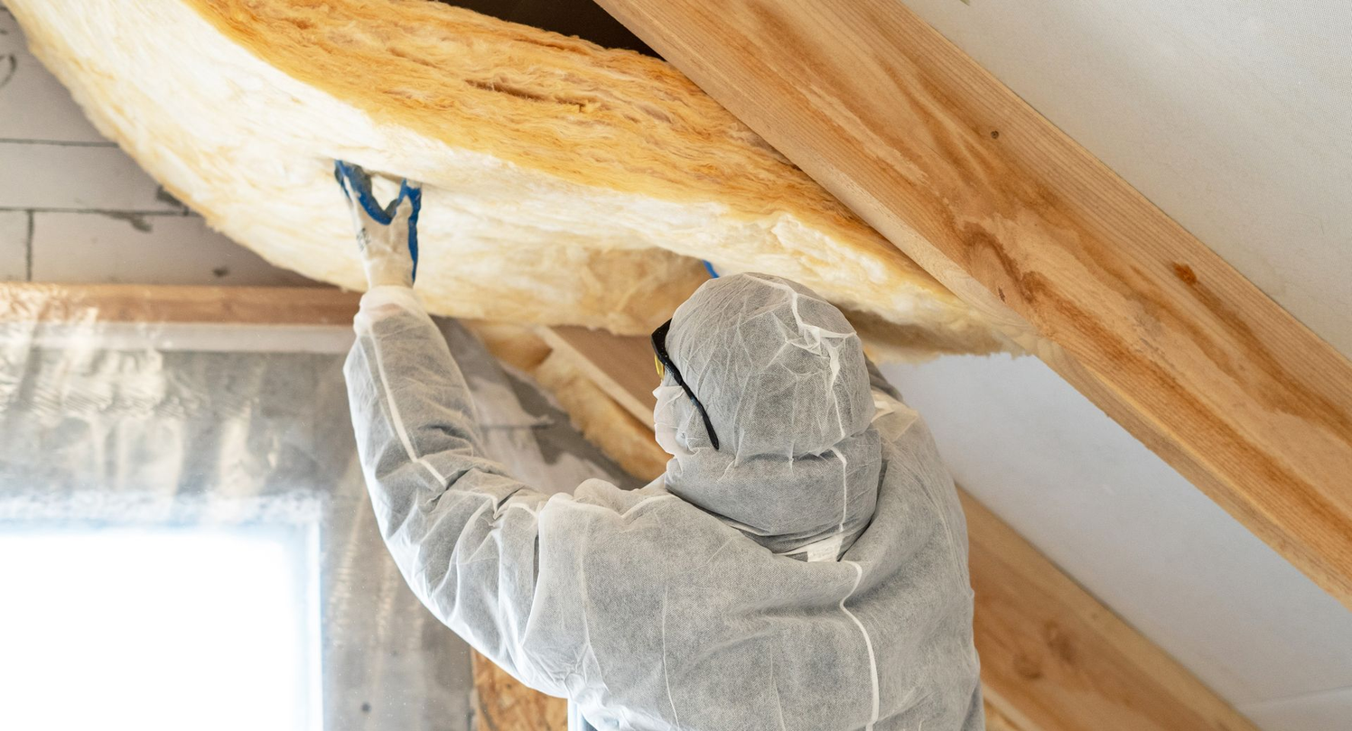 Une personne portant un sweat à capuche gris utilise un outil pour travailler sur des poutres en bois apparentes dans une pièce.