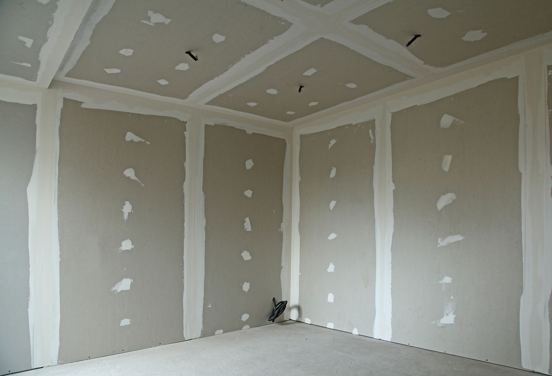 Pièce vide aux murs en plaques de plâtre beiges, joints blancs et plafond nu.