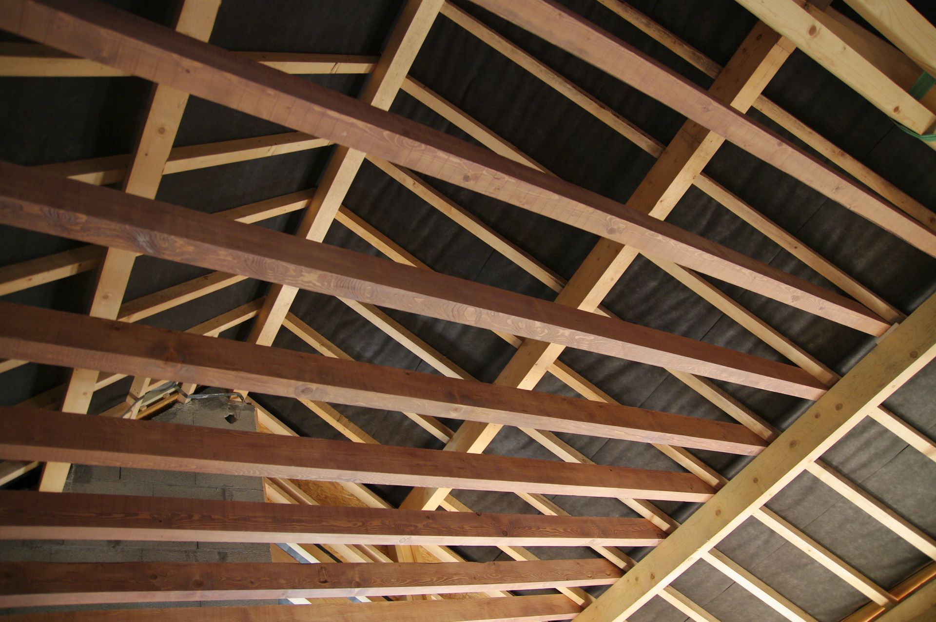 Charpente et chevrons en bois vus d'en bas, avec des panneaux de toiture sombres au-dessus.