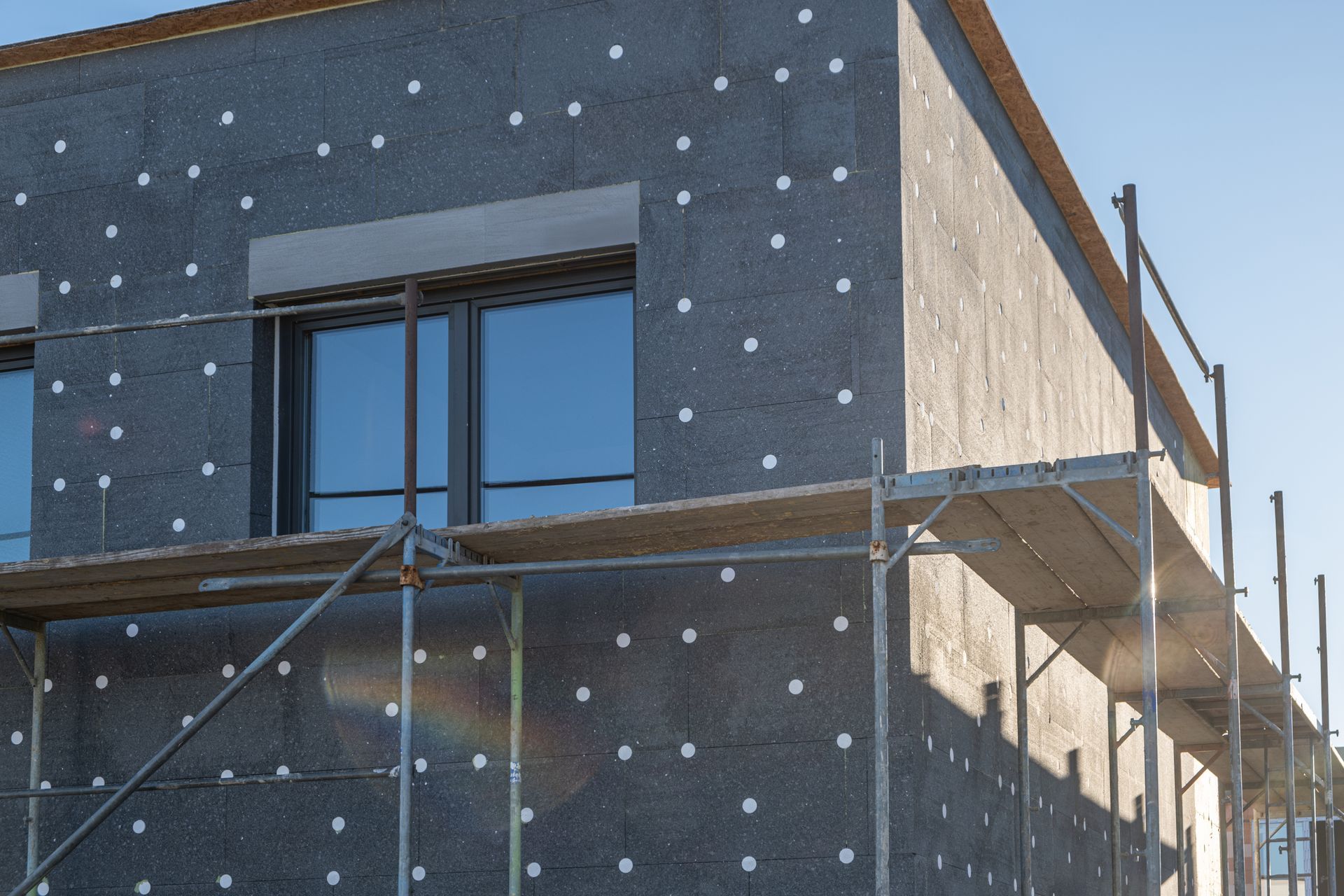 Bâtiment en construction avec échafaudages et panneaux d'isolation à l'extérieur.