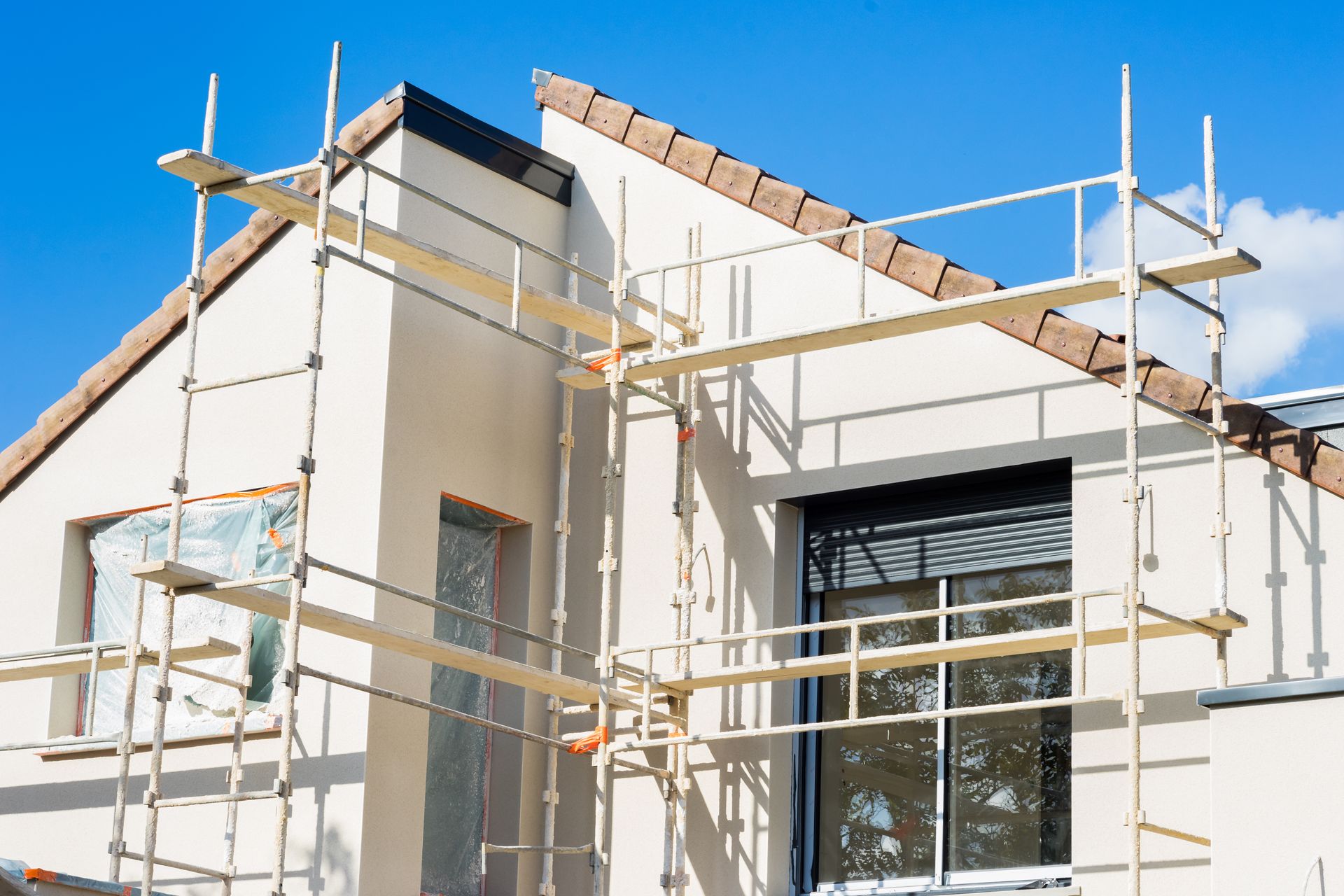 Maison en construction avec des échafaudages autour des murs extérieurs blancs et une grande fenêtre.