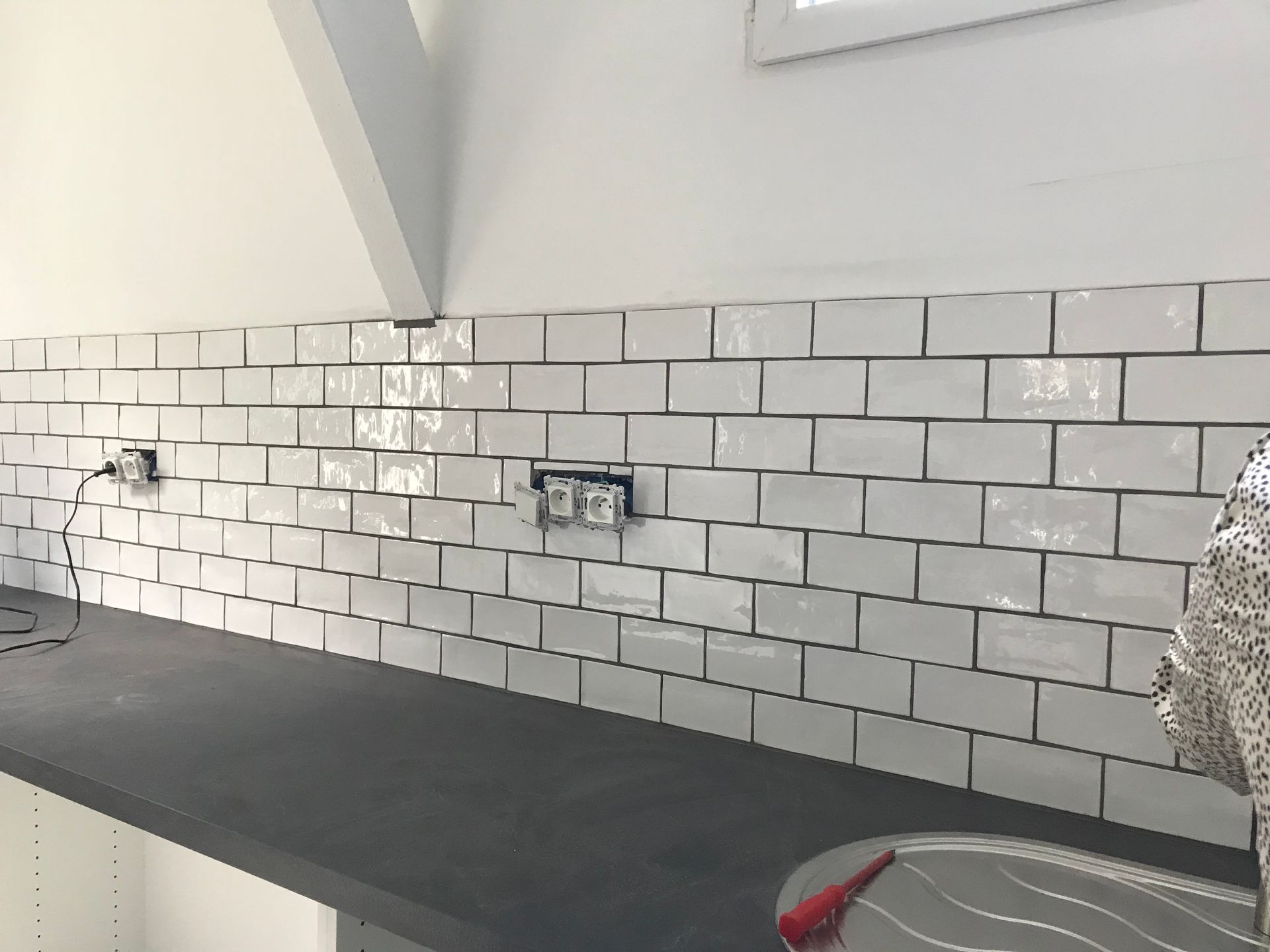 Carrelage mural blanc avec comptoir foncé, prises électriques et mur blanc.