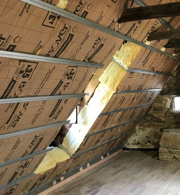 Vue intérieure des combles, isolation par ossature métallique. La lumière naturelle pénètre par une ouverture dans l'isolation.