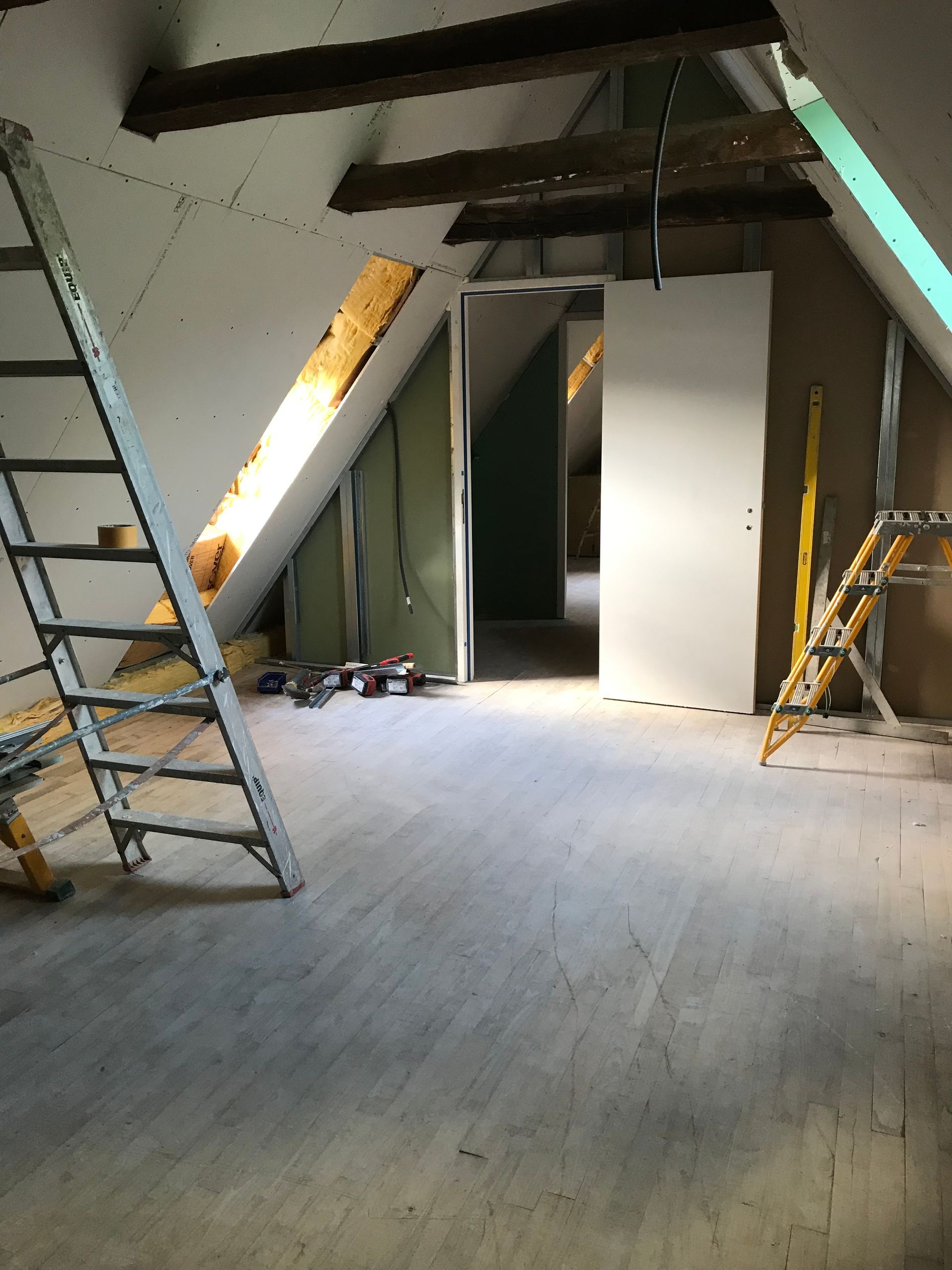 Grenier en construction avec échelle, isolation et murs partiellement finis.