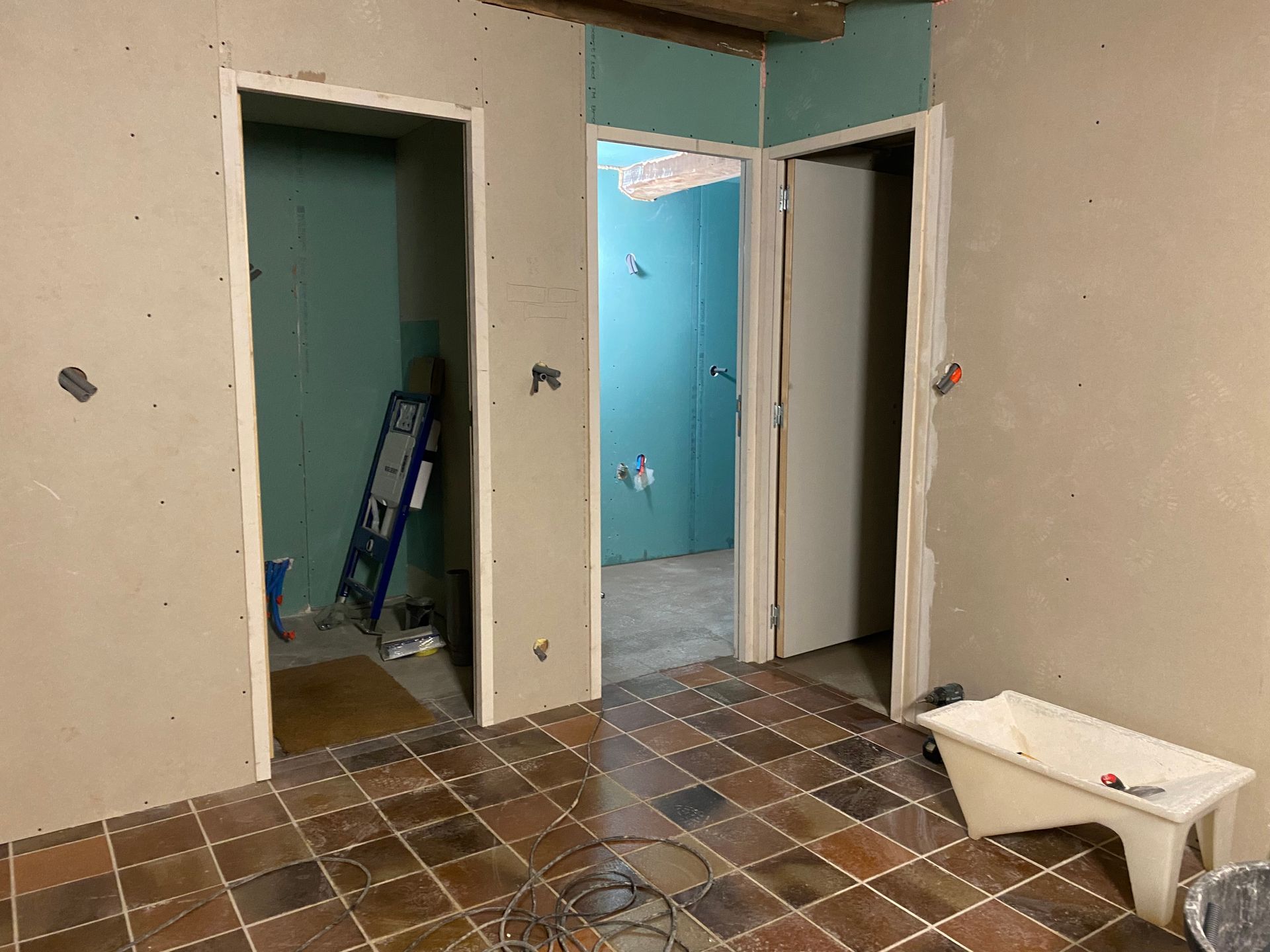 Rénovation d'une pièce intérieure : Deux portes, cloisons sèches apparentes, sol carrelé, une baignoire blanche.