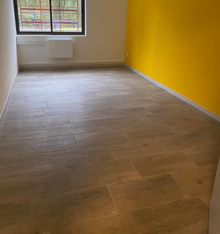 Chambre vide avec sol carrelé marron clair, murs blancs et jaunes, fenêtre avec vue sur la forêt.