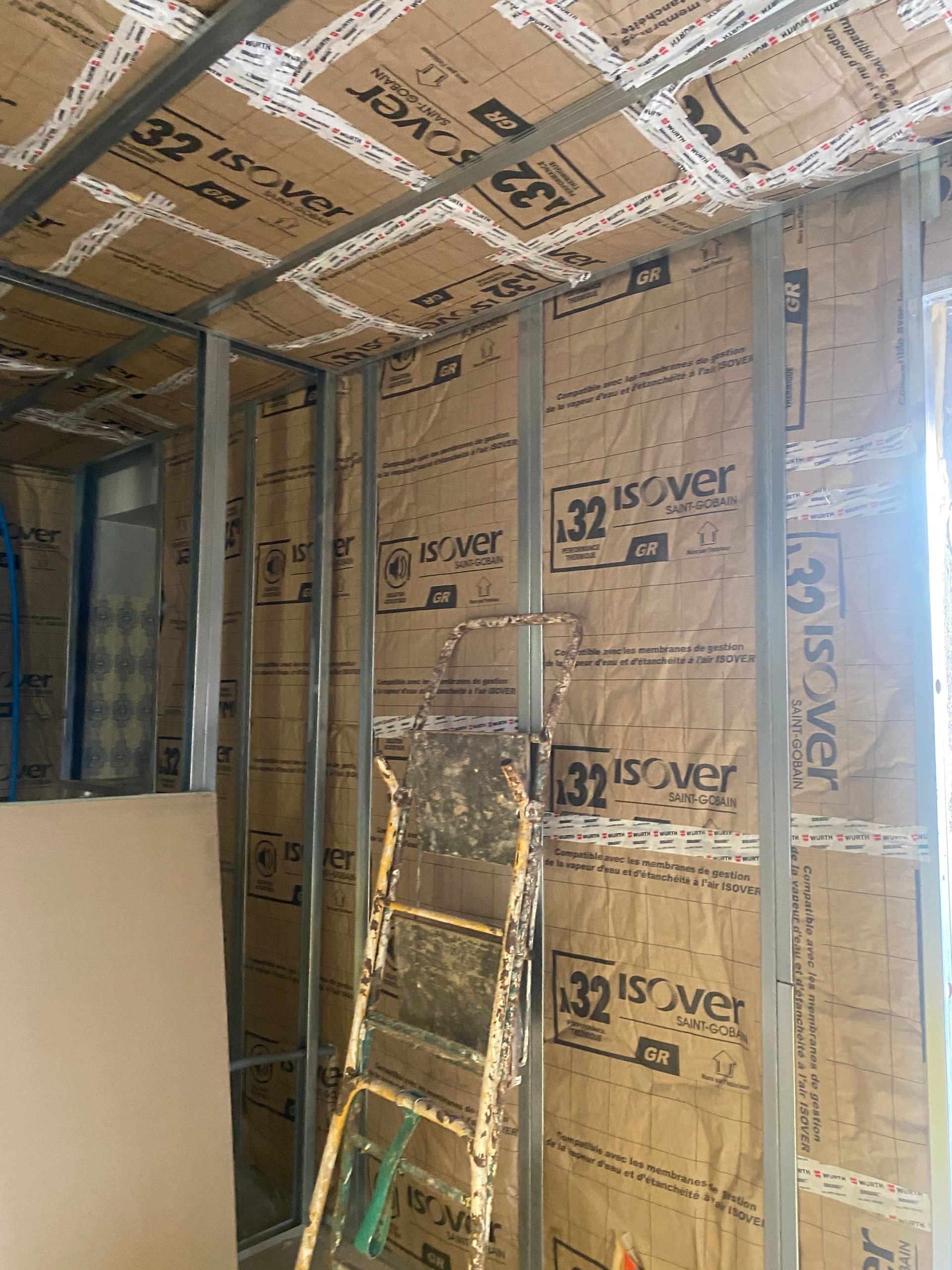 Charpente métallique avec isolation installée, échelle appuyée contre le mur, préparation pour les cloisons sèches.