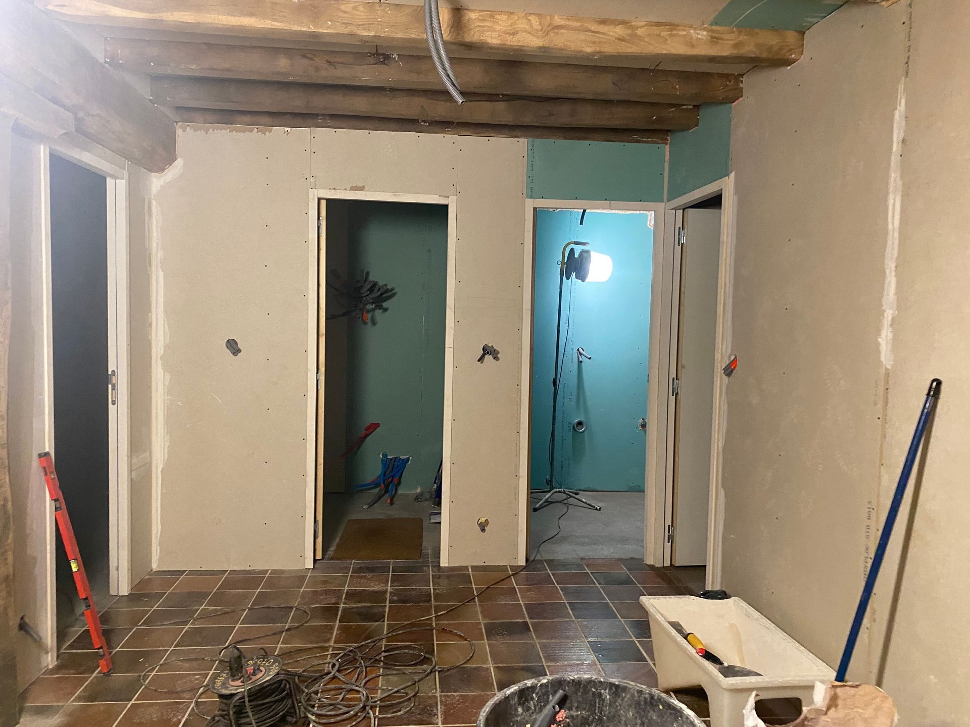 Rénovation intérieure : portes en cloisons sèches; poutres apparentes au plafond; sol en carrelage rouge.