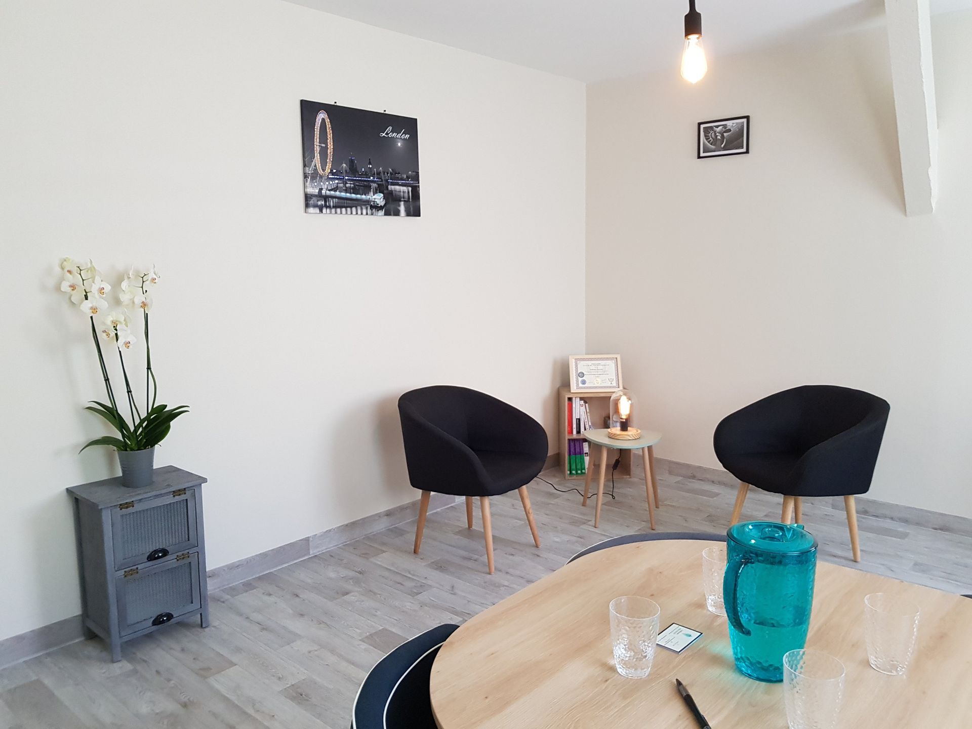 Salle de thérapie avec deux chaises noires, une table et une table d'appoint avec une plante.