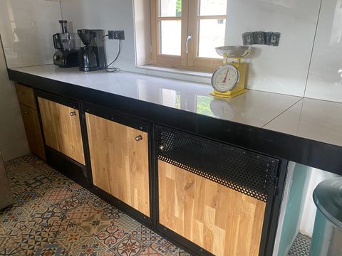 Cuisine avec armoires en métal noir, portes en bois, comptoir clair et fenêtre.