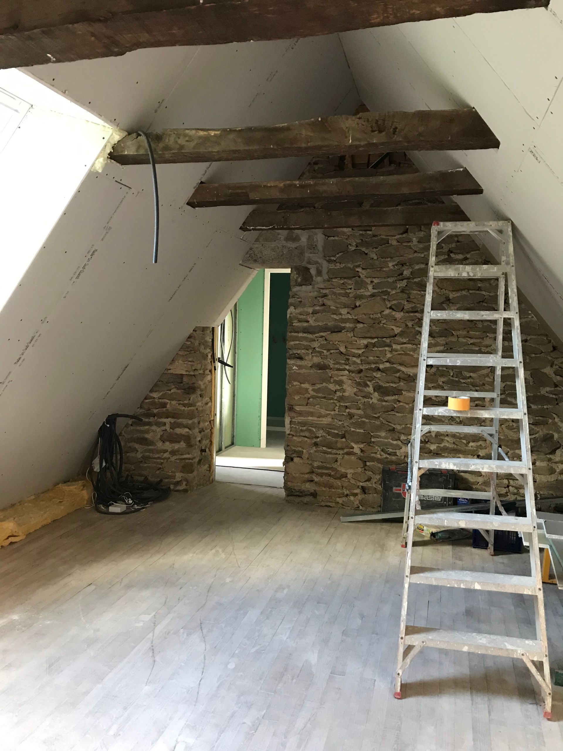 Grenier rénové avec mur en pierre, poutres en bois, échelle.