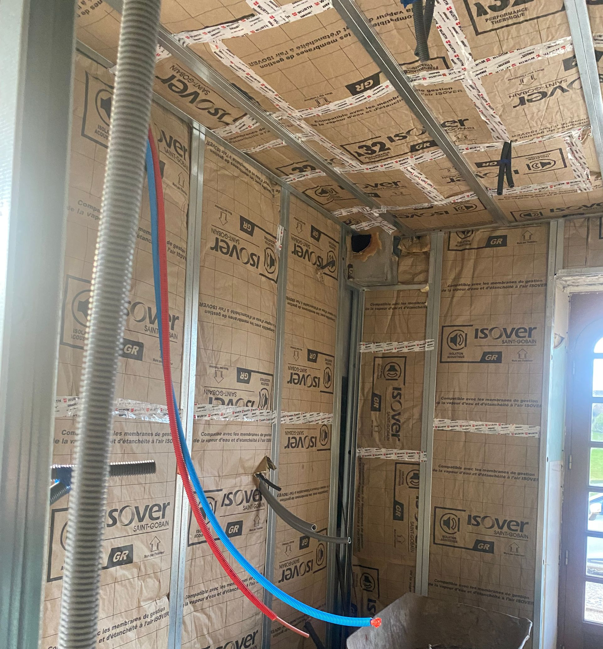 Aménagement intérieur : charpente métallique, isolation, tuyaux bleus et rouges, conduit électrique.