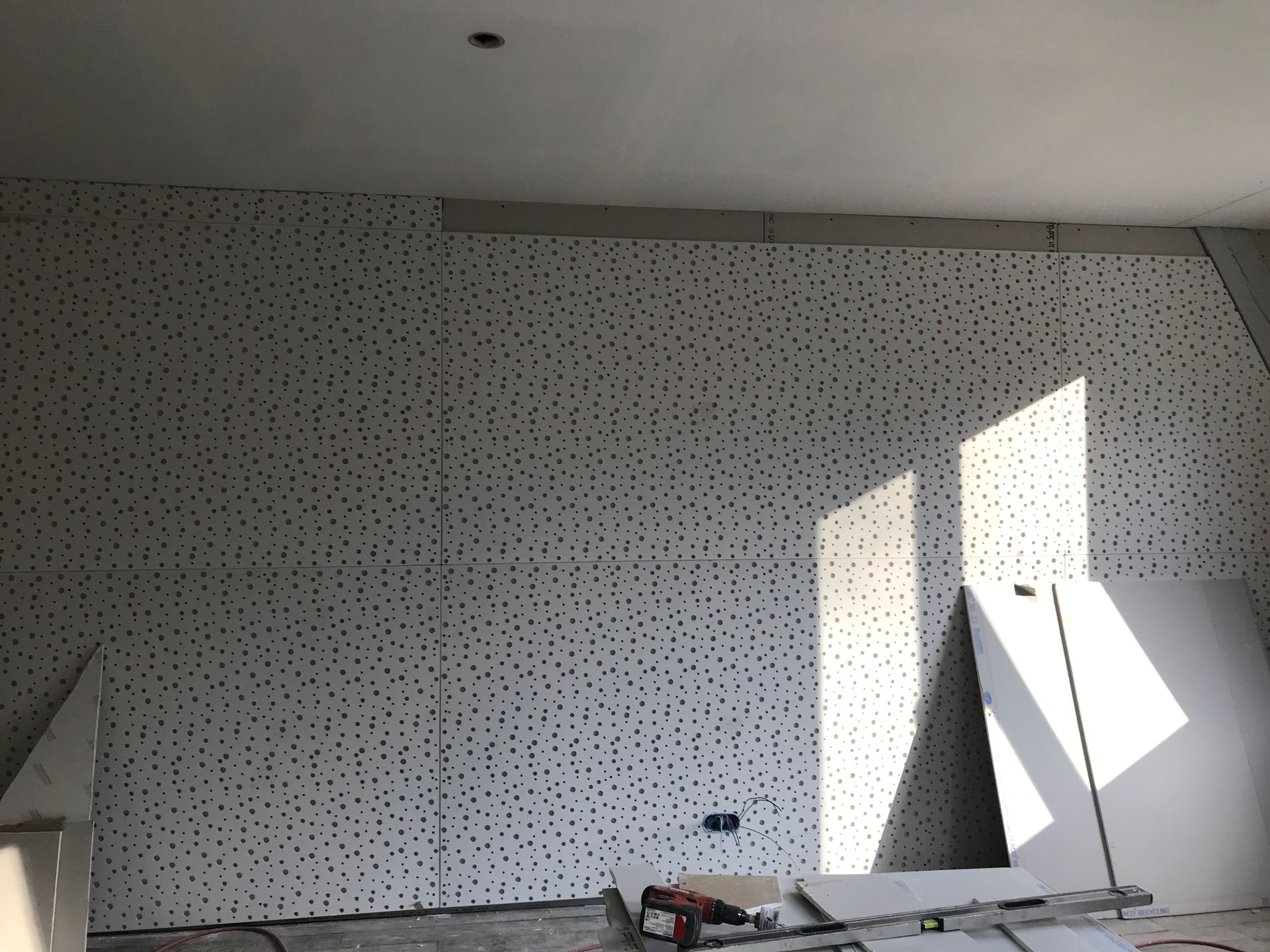 Salle intérieure en construction, avec des panneaux insonorisants perforés sur les murs. La lumière du soleil filtre à travers la structure inachevée.