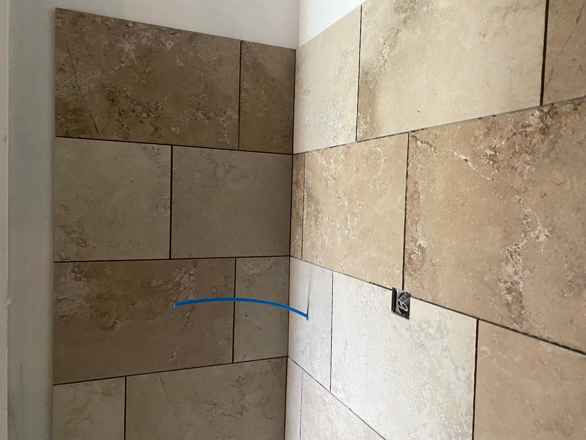 Murs carrelés dans les tons beige et beige, avec une prise électrique visible dans le coin.