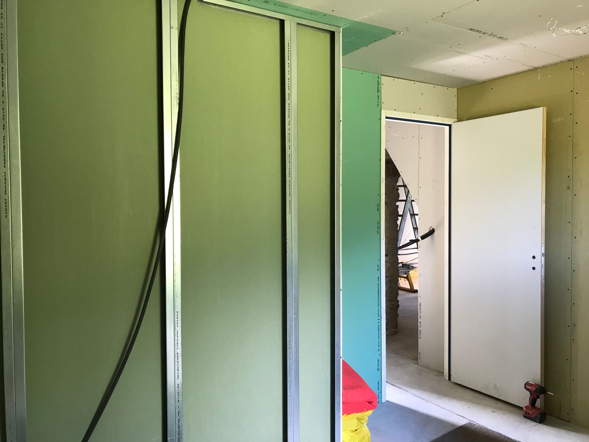 Pièce intérieure aux cloisons sèches vertes. Une porte blanche est visible sur une porte ouverte.