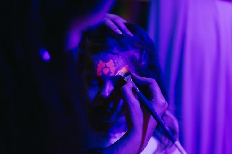 Una persona a la que le están pintando la cara bajo luces de escenario moradas