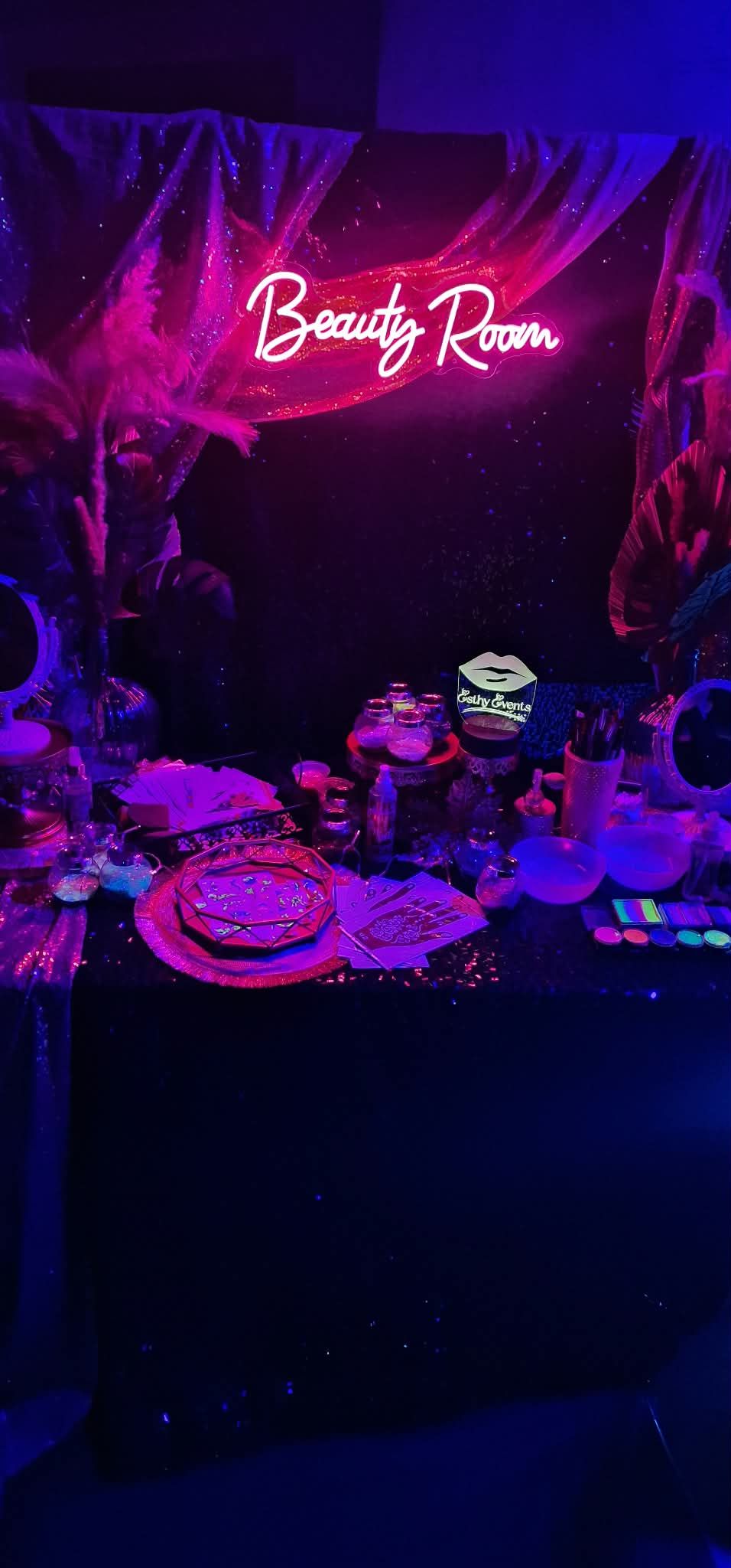 Letrero rosa neón de “Salón de Belleza” brillando sobre una mesa oscura iluminada en púrpura con platos y decoración.