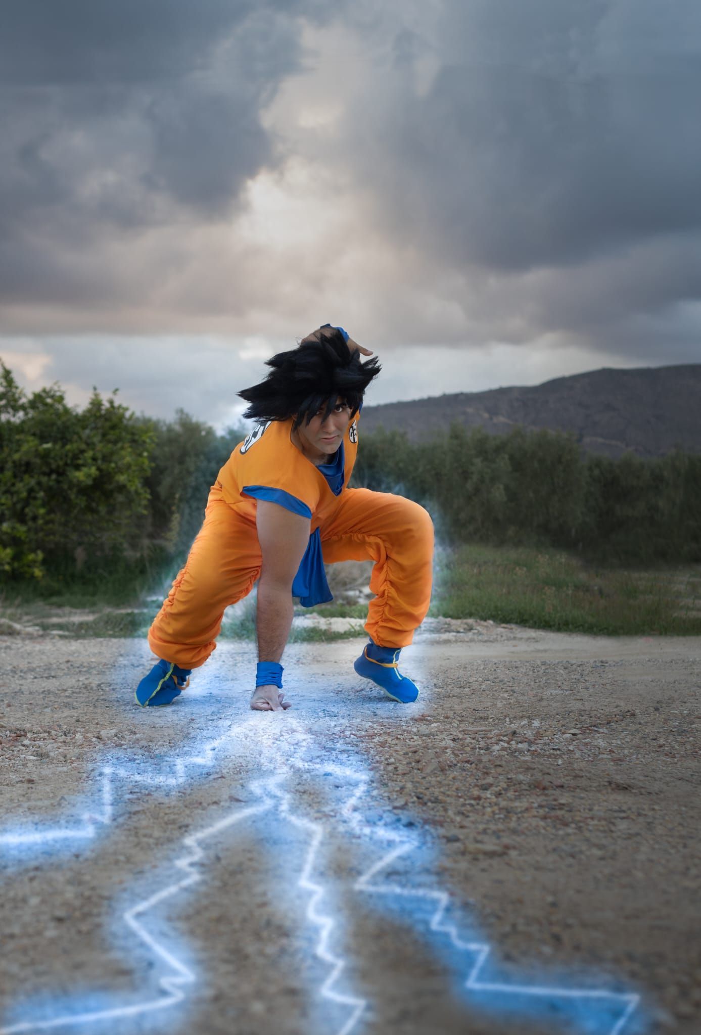 Una persona vestida de naranja y azul se agacha en una carretera mientras un rayo azul cruza el suelo.