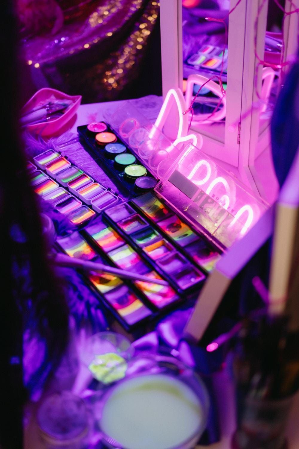 Paleta de maquillaje y brochas iluminadas con neón rosa-violeta sobre un tocador.
