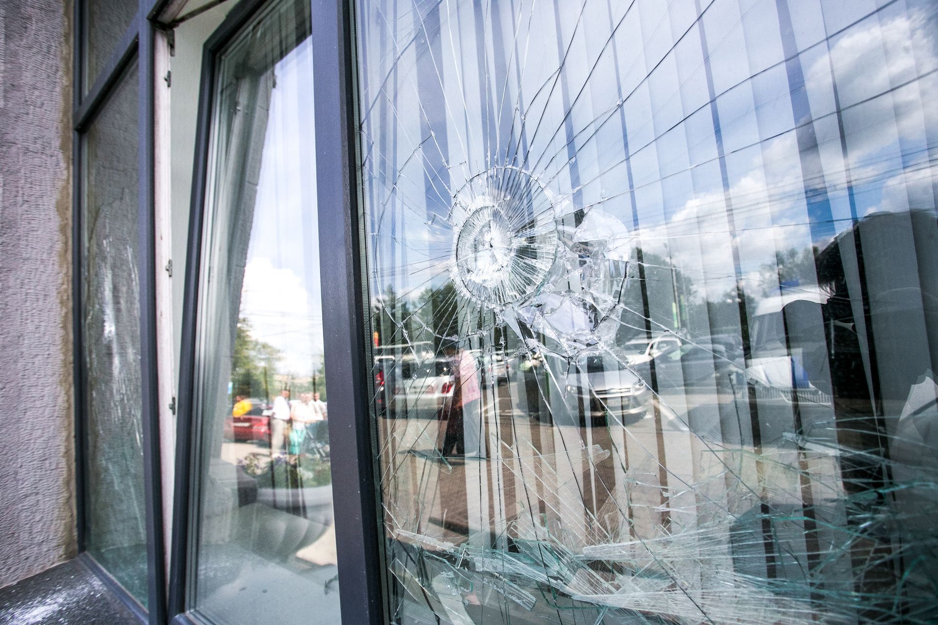 Vitrine fissurée reflétant la rue et le ciel nuageux