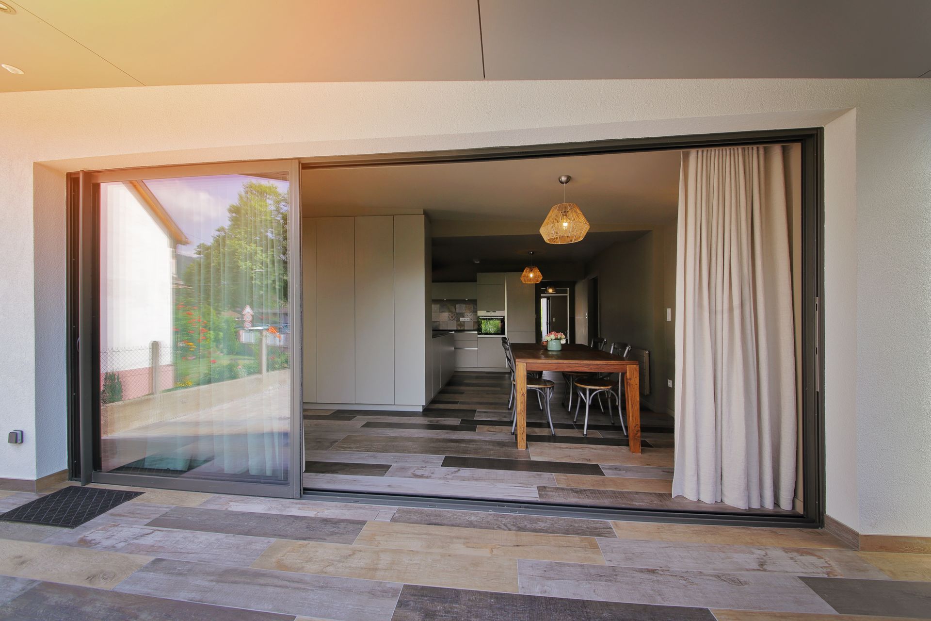 Baie coulissante de maison ouverte sur une pièce de vie moderne avec table en bois