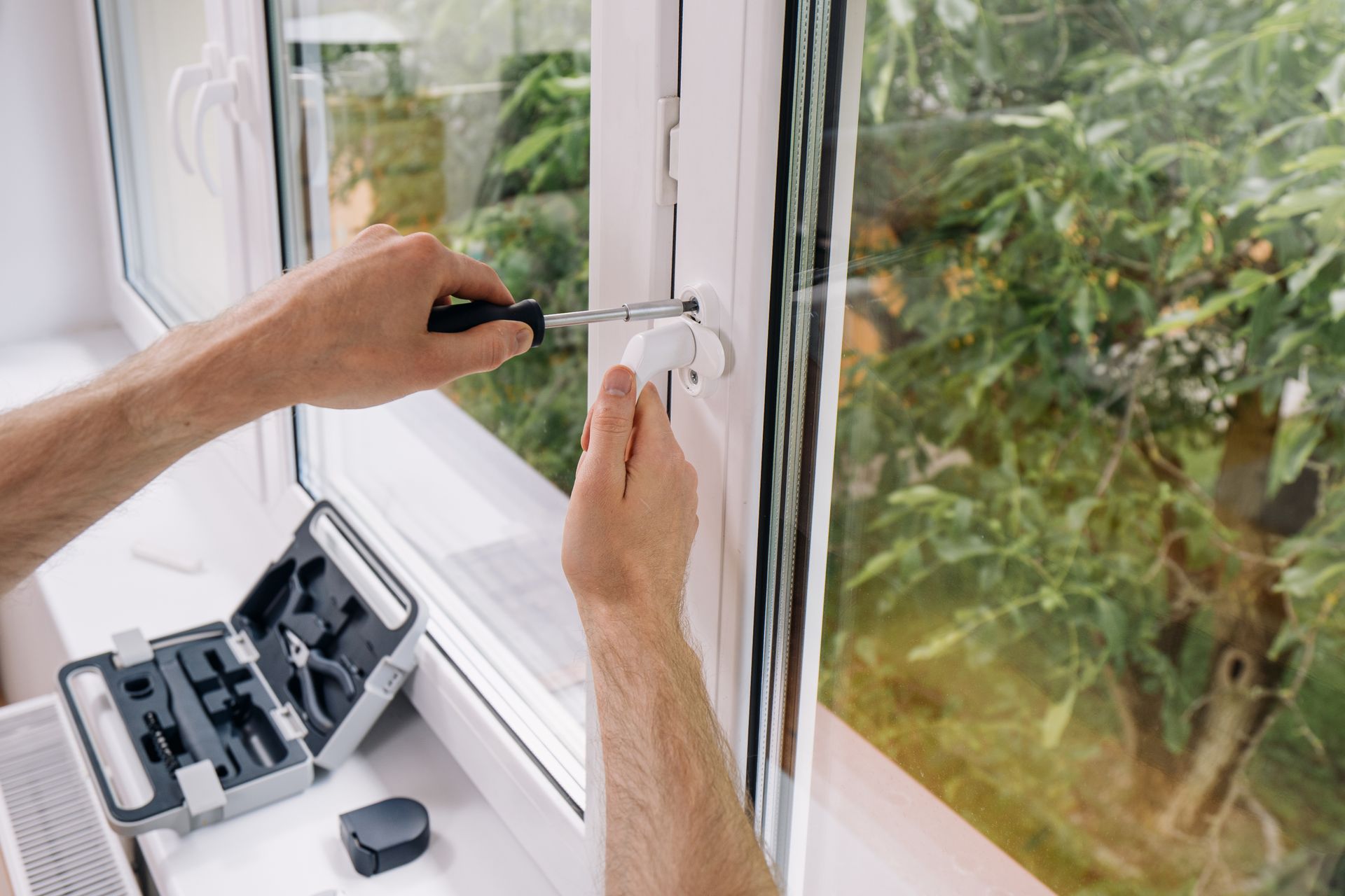 Des mains installent un loquet de fenêtre blanc avec un tournevis à côté d'une boîte à outils ouverte