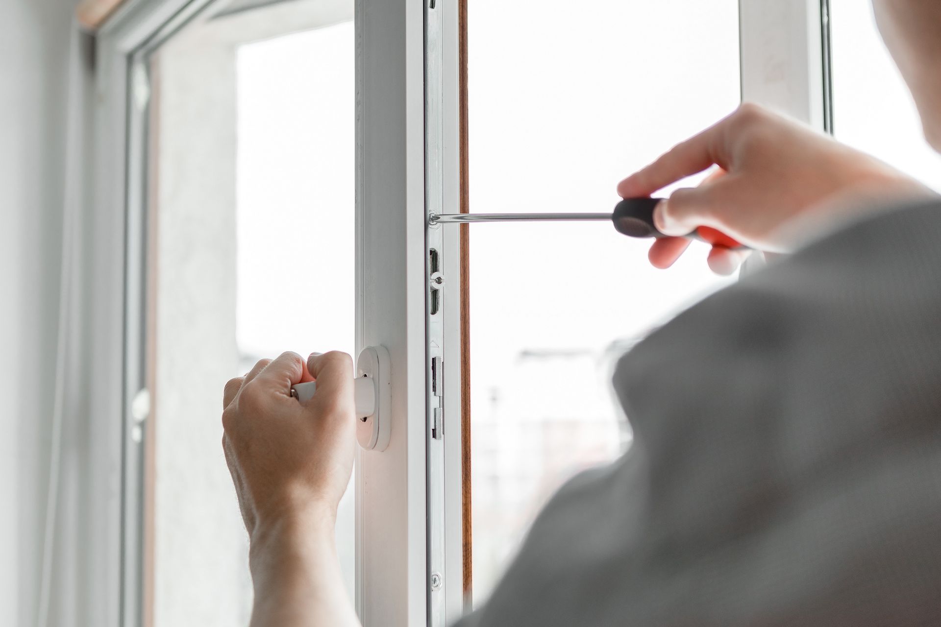 Des mains utilisent un tournevis pour régler le loquet d'une fenêtre sur un cadre blanc