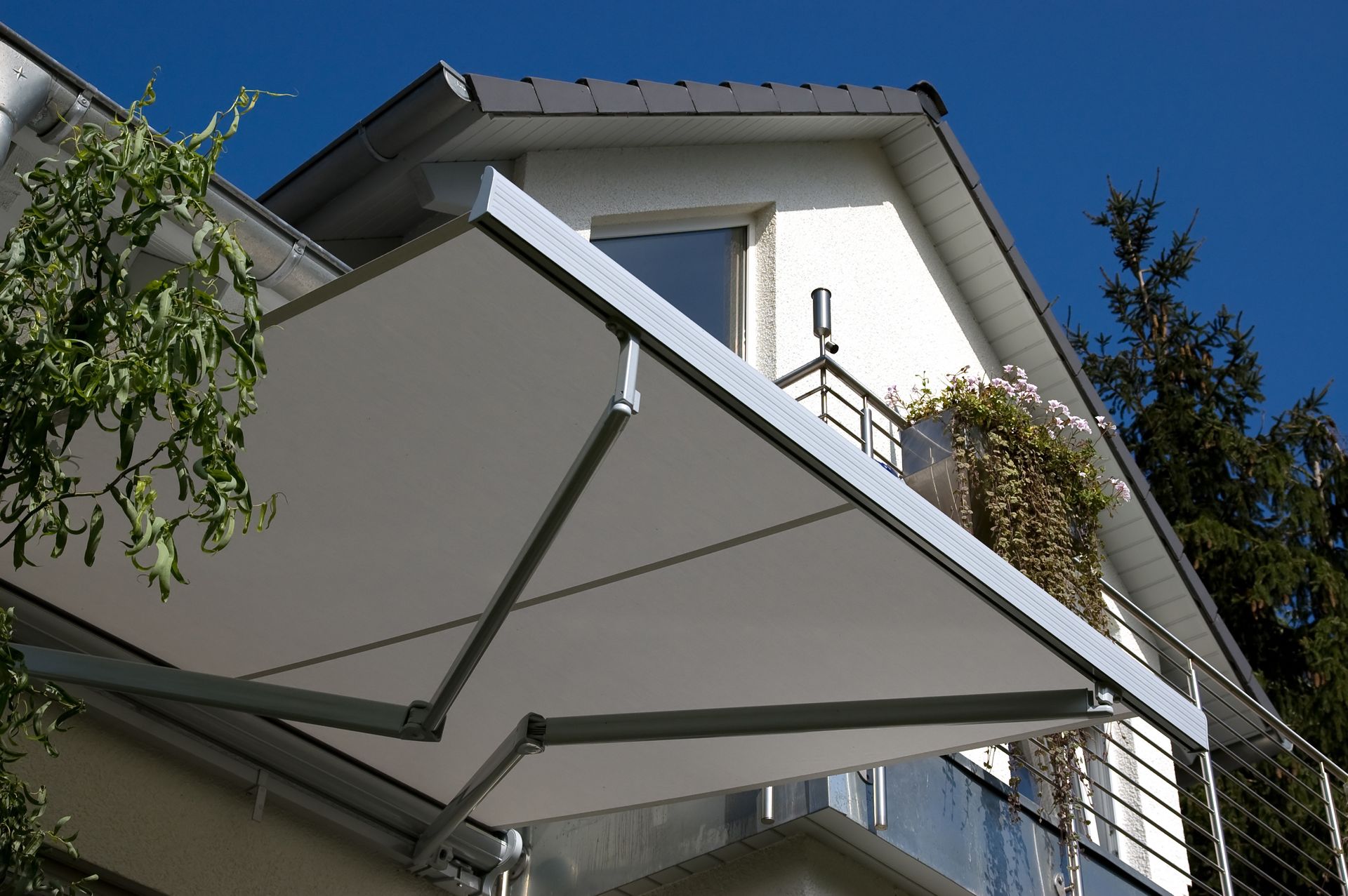 Store banne blanc à structure métallique, avec maison et balcon en arrière-plan