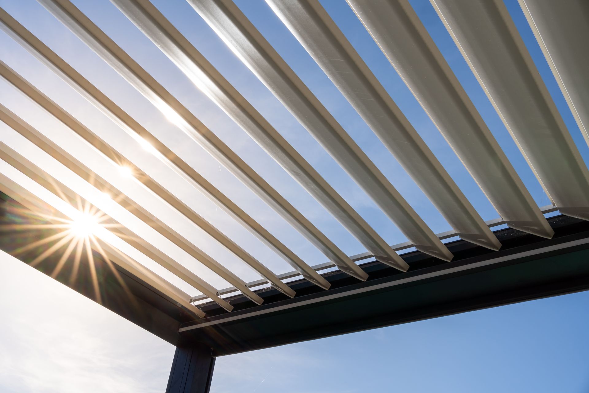 La lumière du soleil filtrant à travers les lames blanches d'une pergola sur un ciel bleu