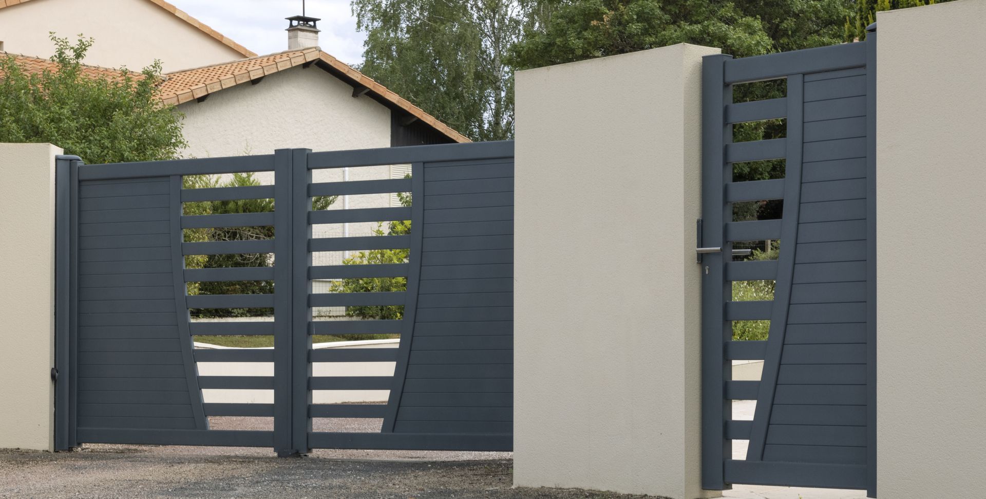 Portail d'allée moderne en métal gris avec lattes horizontales, jouxtant un mur et une maison