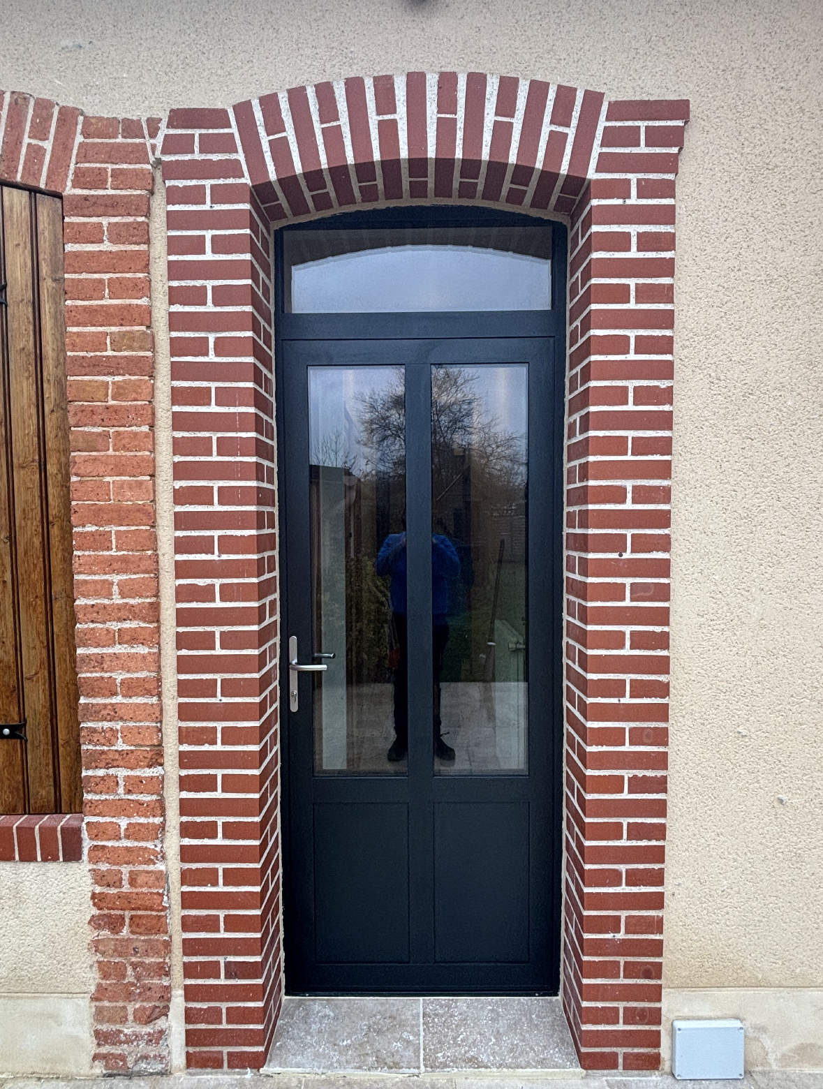 Porte d'entrée vitrée sombre avec encadrement de porte en briques rouges