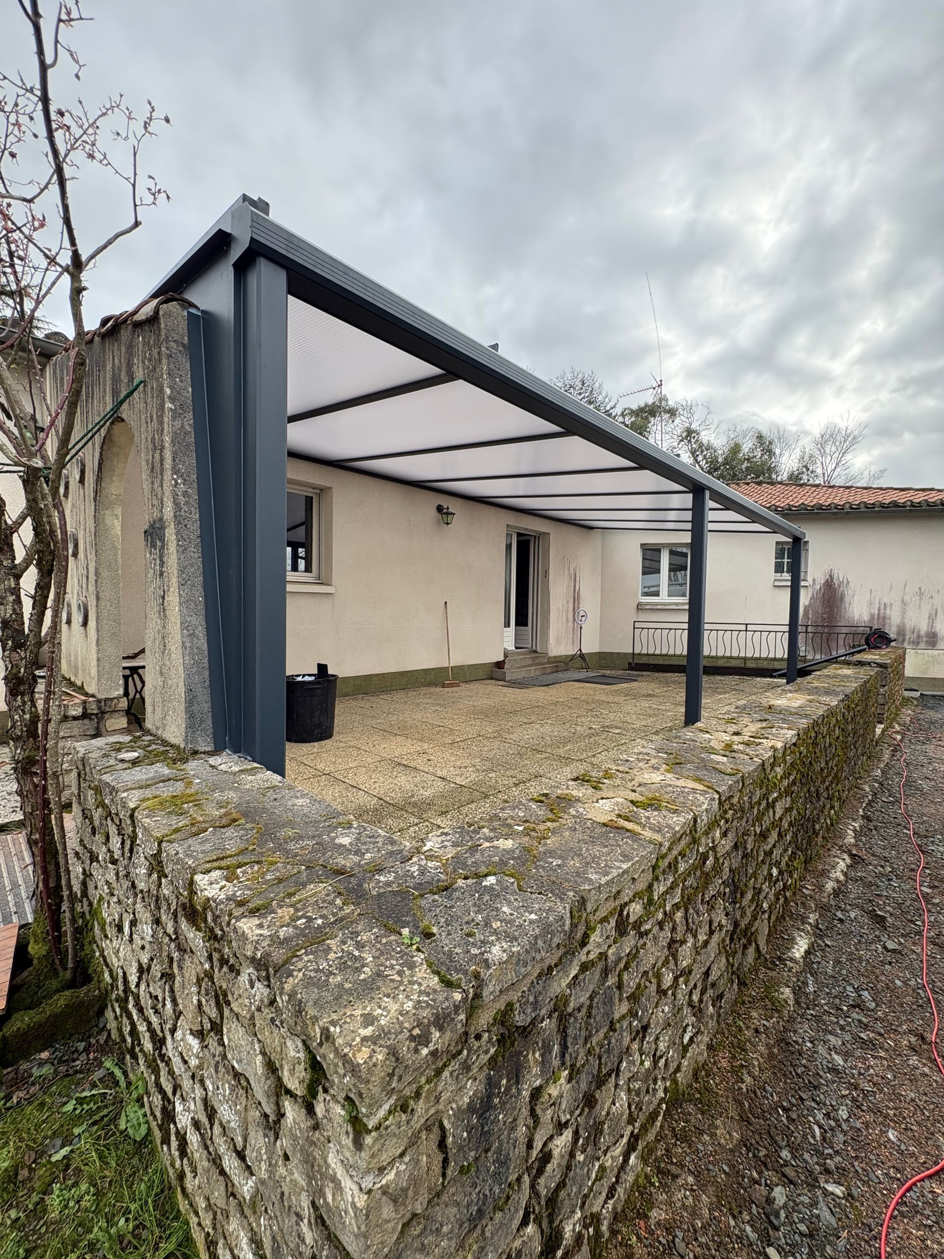 Terrasse en pierre avec une pergola blanche et anthracite attenante à une maison