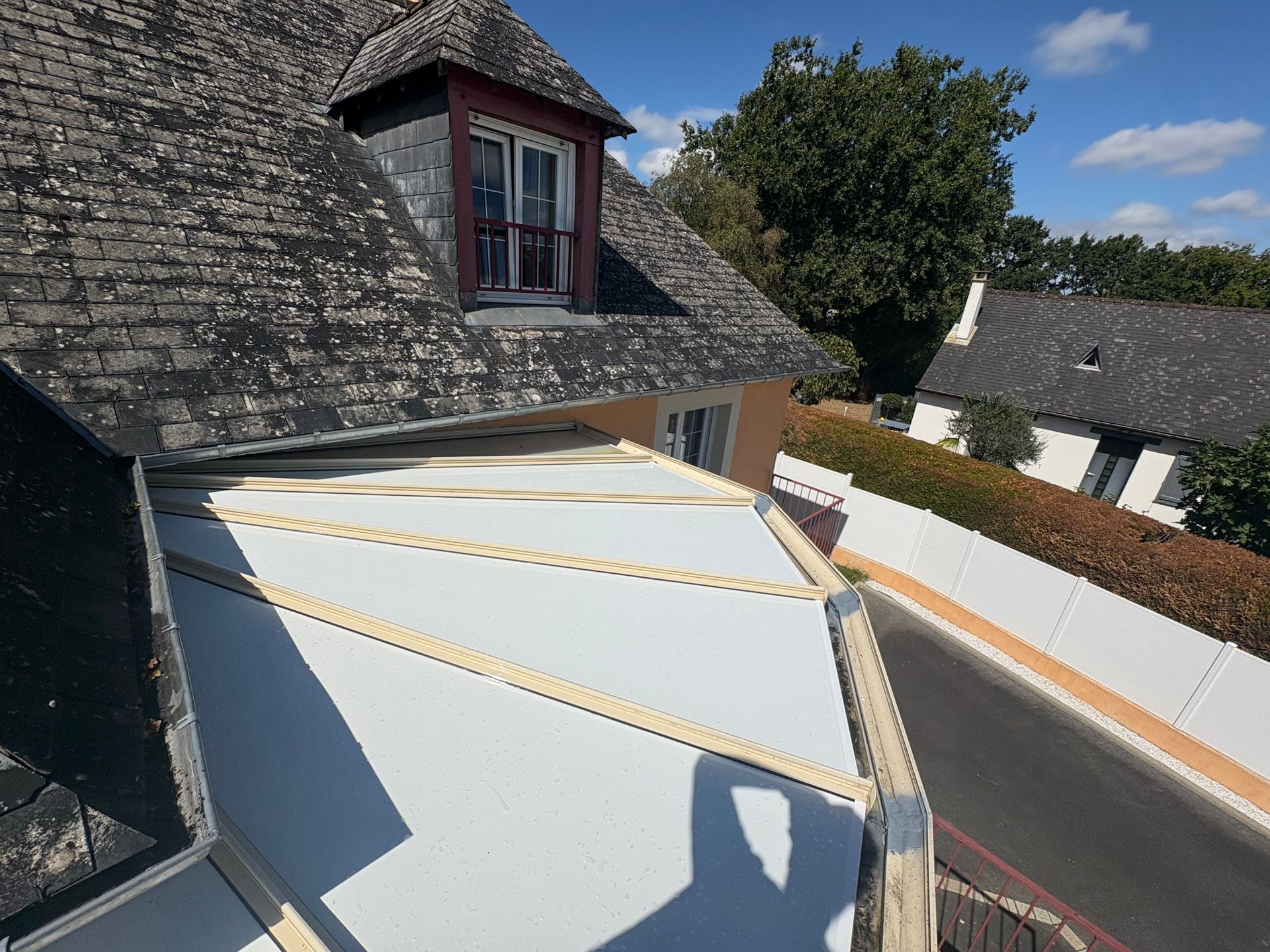 Panneaux blancs de la toiture d'une véranda à côté d'une toiture de maison faite en ardoise