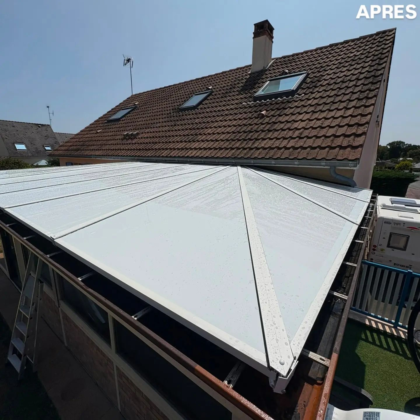 Panneaux de toiture blancs sur une véranda, à côté d'un toit de tuiles brunes disposant de fenêtres de toit