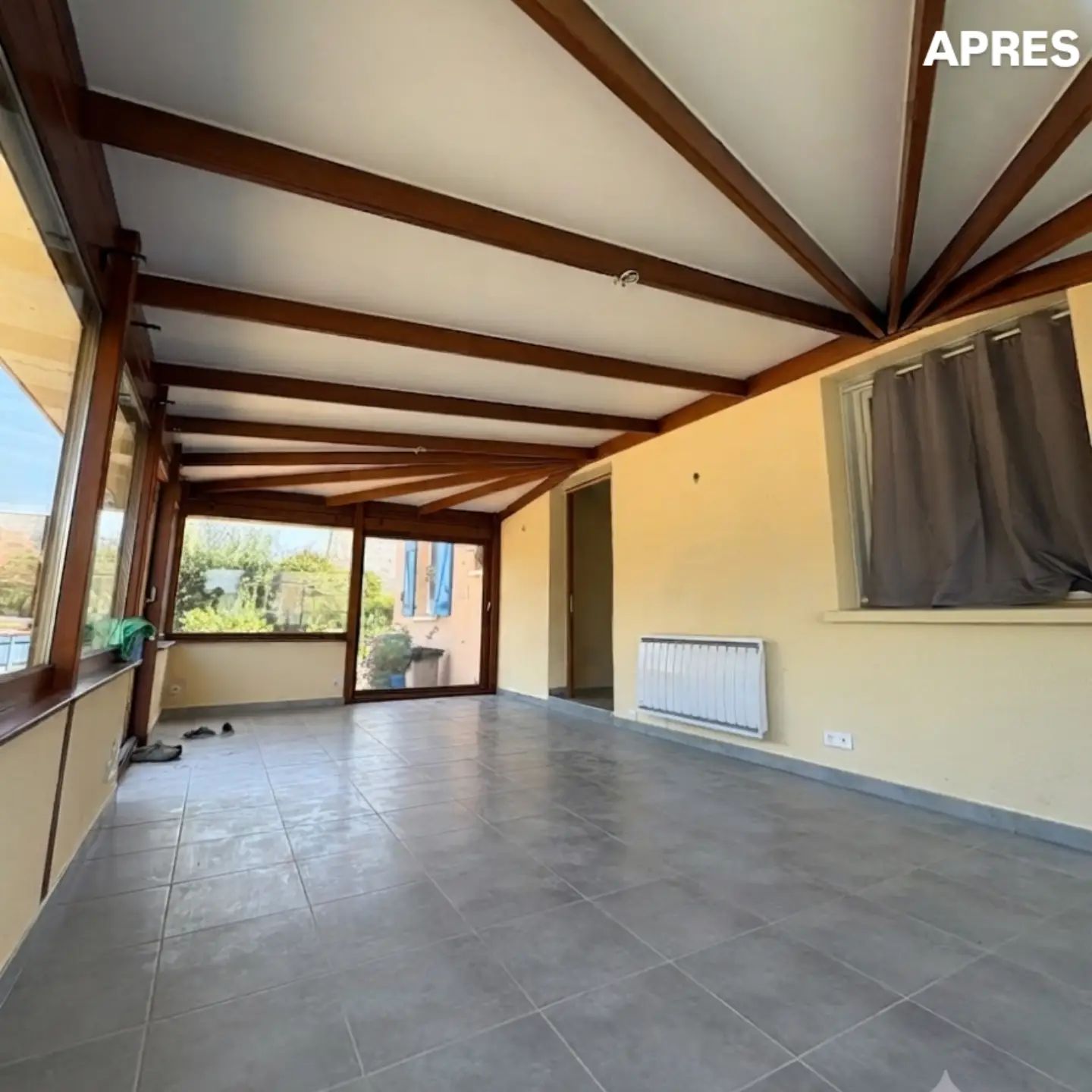 Intérieur d'une véranda de maison avec mur jaune, radiateur et rideau de fenêtre