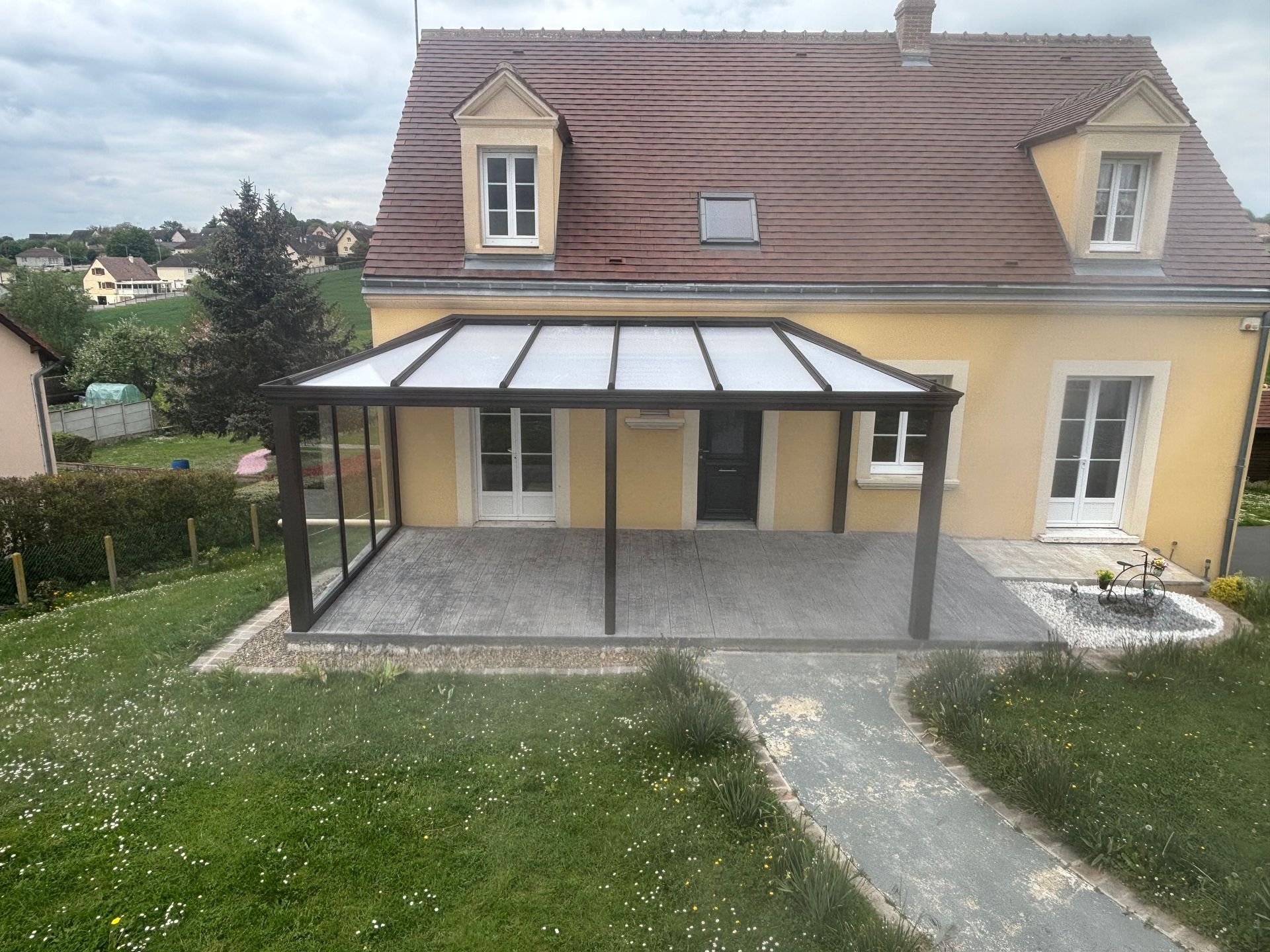 Maison jaune avec un patio couvert et un chemin de pierre traversant la pelouse