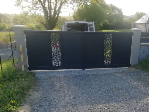 Portail de maison métallique encadré par des piliers en béton, donnant sur un chemin d'accès