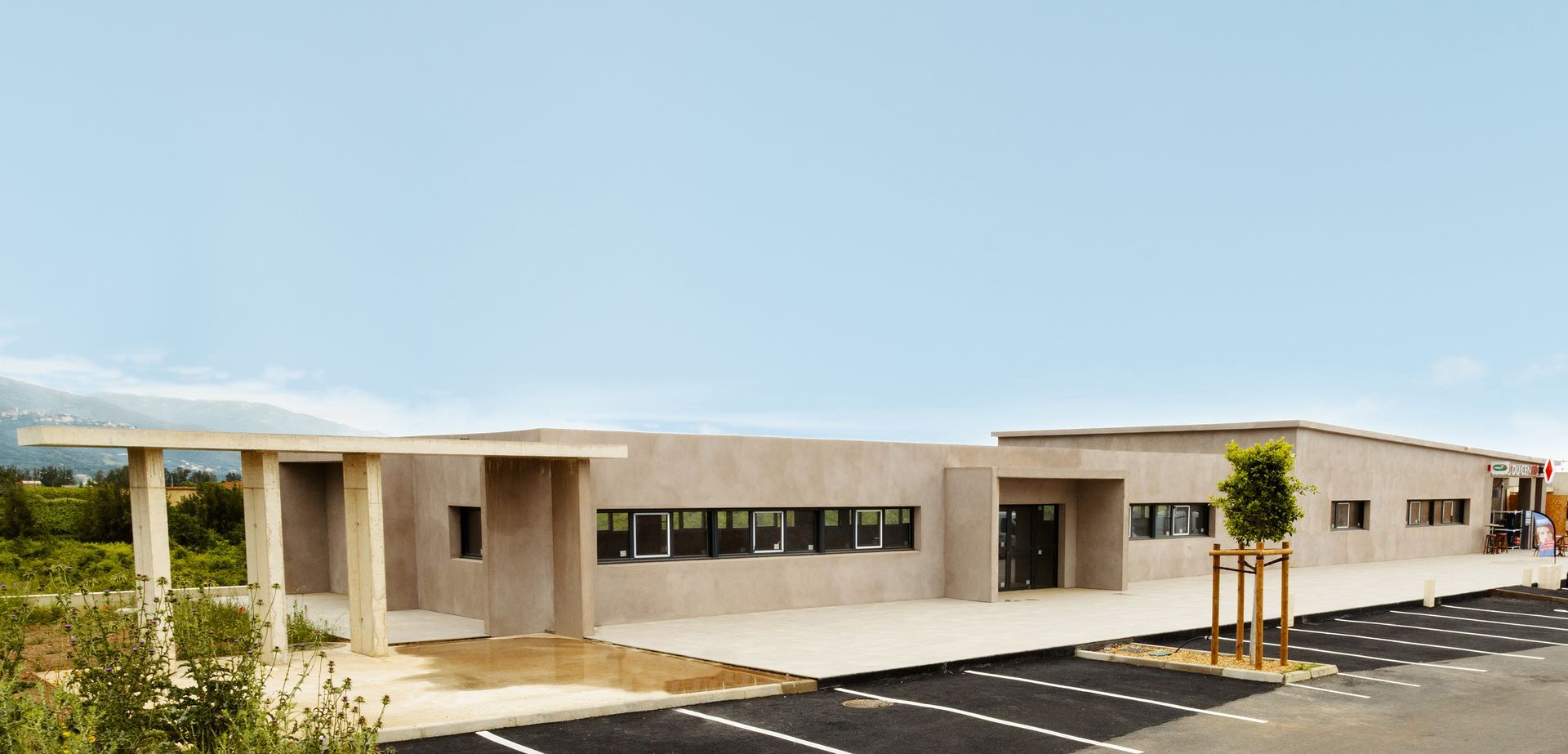 Bâtiment beige moderne avec abri voiture, fenêtres et parking. Extérieur avec ciel bleu.