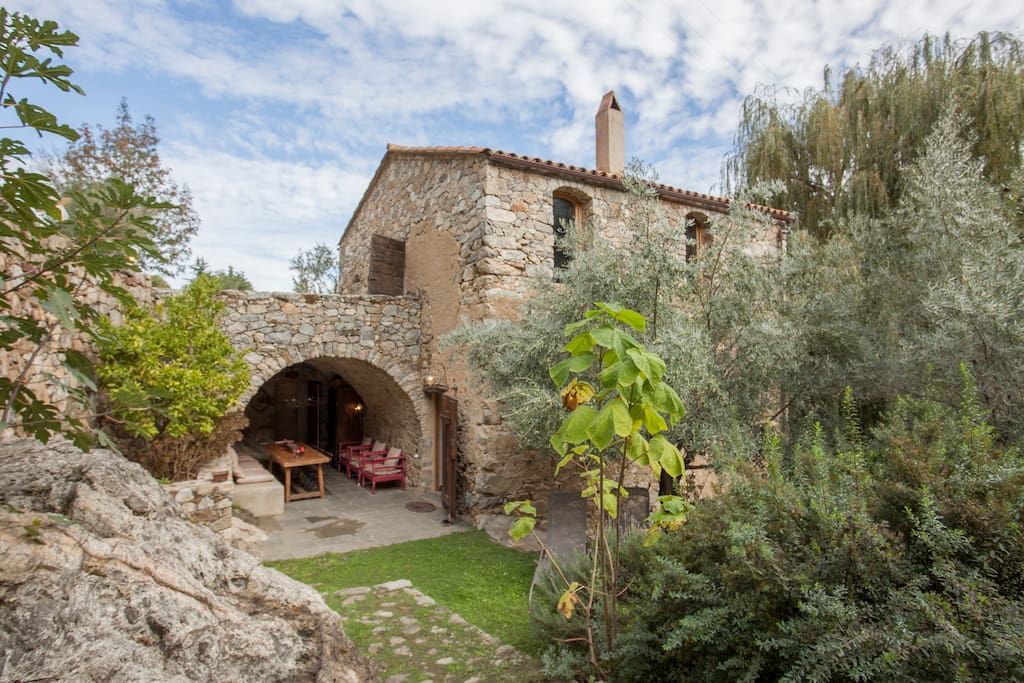 Maison en pierre avec entrée voûtée, nichée dans un écrin de verdure.
