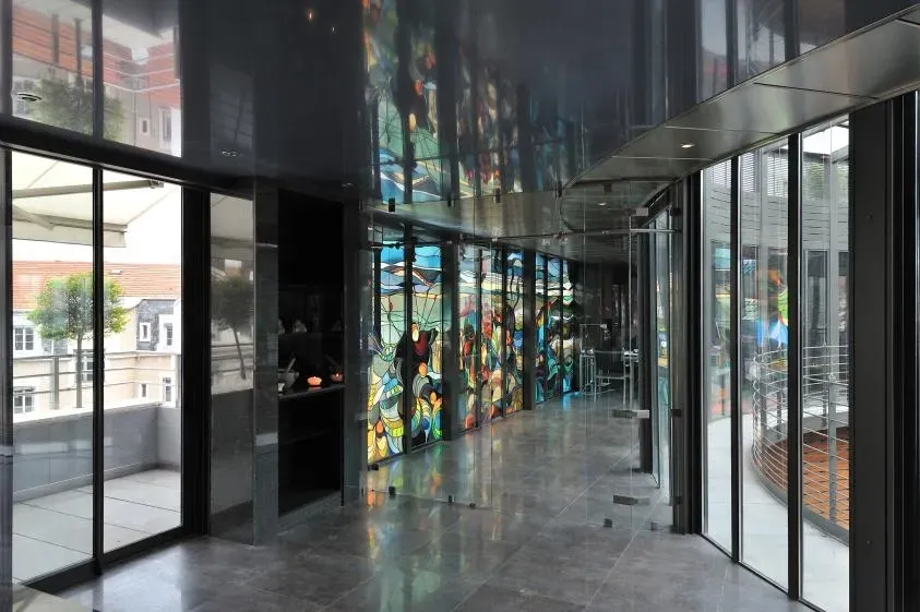 Couloir moderne avec mur en vitrail coloré, portes vitrées et plafond en miroir.