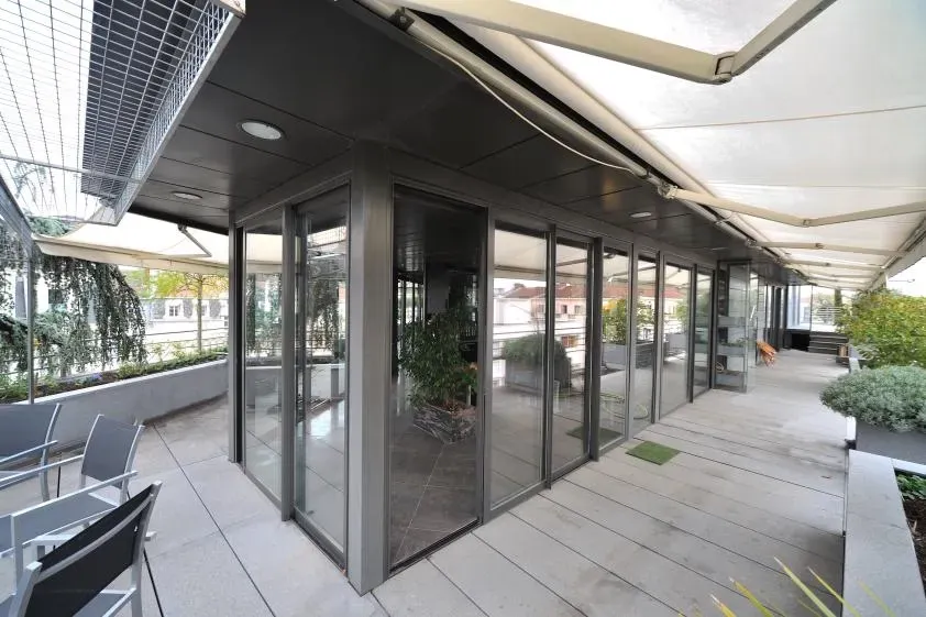 Terrasse sur le toit avec structure vitrée, auvents et végétation. 