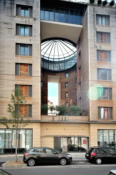 Immeuble d'appartements moderne avec une grande ouverture circulaire. Voitures garées devant.