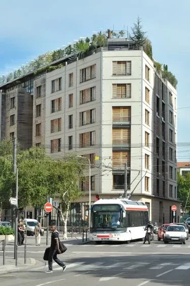 Un immeuble à plusieurs étages avec un jardin sur le toit et un trolleybus dans une rue de la ville.