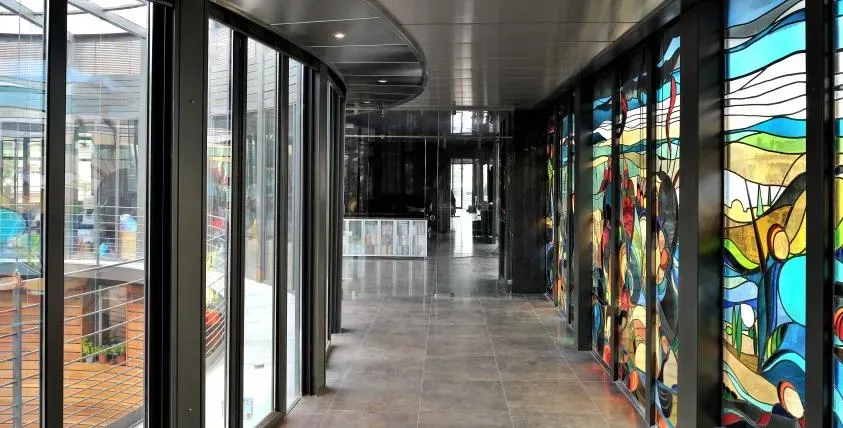 Un couloir incurvé avec des vitraux et des panneaux de fenêtre, menant à un mur lointain en miroir.