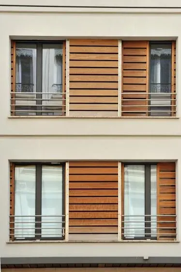 Deux étages d'un immeuble d'appartements avec fenêtres, volets en bois et balustrades en métal.