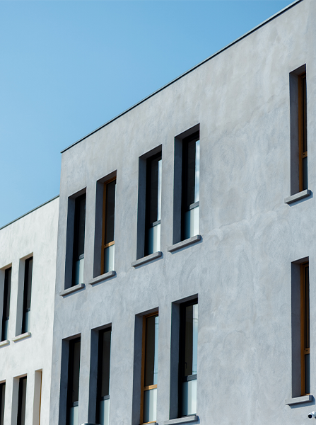 Bâtiment blanc moderne avec des rangées de fenêtres hautes et étroites à cadre noir contre un ciel bleu clair.