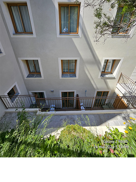 Vue extérieure d'un bâtiment avec fenêtres, balcon et végétation devant. 